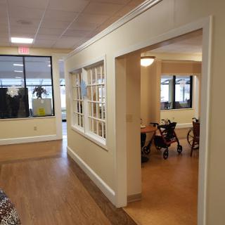 A well-lit interior hallway leading to an office space, featuring large windows and a warm wooden floor.