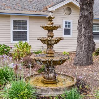 A three-tiered fountain stands in a landscaped garden in front of a house.