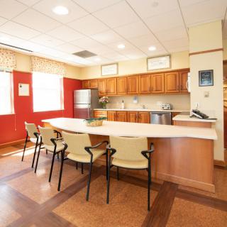 A modern kitchen and meeting area with wooden cabinetry and a central counter surrounded by chairs.