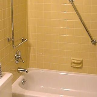 A vintage-style bathroom with yellow tiled walls and a white bathtub equipped with a grab bar.