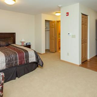 A cozy bedroom featuring a large bed with a patterned comforter, carpeted flooring, and an open closet in the background.
