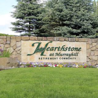 A sign for Hearthstone at Murrayhill Retirement Community surrounded by a stone wall and greenery.