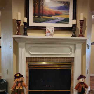 A cozy fireplace decorated with autumn-themed items, including scarecrow figures and candles on the mantel.