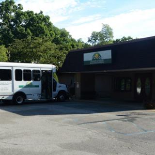A shuttle bus parked outside a building surrounded by trees.