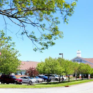 A sunny day view of a building surrounded by trees and parked cars.