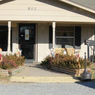 A small house with a porch and flower beds at the entrance.