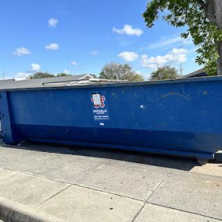 A blue dumpster on the side of the street under a clear sky.