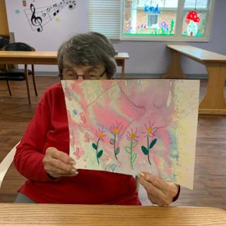 An elderly person proudly displaying their colorful floral painting.
