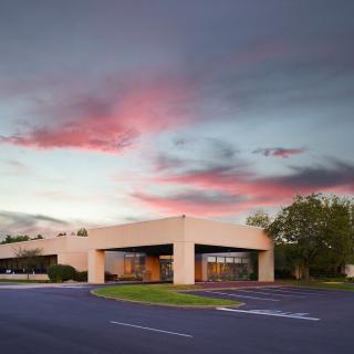 A modern building under a colorful sunset sky with clouds, surrounded by a parking lot.
