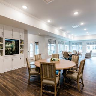 A modern and spacious dining area featuring a large table surrounded by chairs, illuminated by bright lighting.