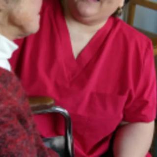 A caregiver in a red uniform assisting an elderly person.