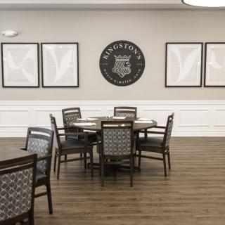 A minimalist dining area with wooden tables and chairs, featuring decorative wall art and a polished wooden floor.