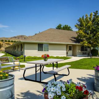 A peaceful backyard setting with a picnic table, surrounded by flowers and trees on a sunny day.