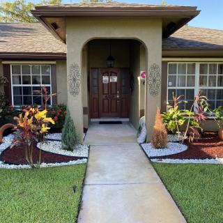 A well-maintained front yard with a pathway leading to the entrance of a house, surrounded by landscaped gardens.