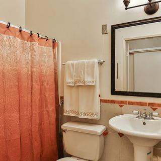 A cozy bathroom featuring a pedestal sink, mirror, toilet, and a peach-colored shower curtain.