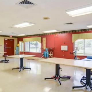 An empty classroom featuring tables and chairs with large windows allowing natural light.