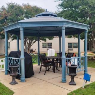 A blue gazebo with outdoor seating and a covered grill, set in a garden area.