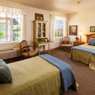 A cozy bedroom with two twin beds, decorated with elegant furniture and large windows.