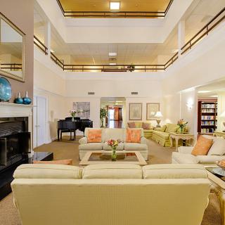 A spacious and elegantly decorated living room with multiple seating areas, a grand piano, and a fireplace.