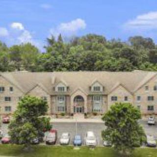 A three-story residential building with a parking lot and surrounded by trees.