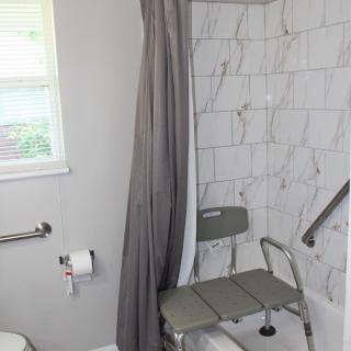 A bathroom with a tiled shower area featuring a shower chair and grab bar for accessibility.