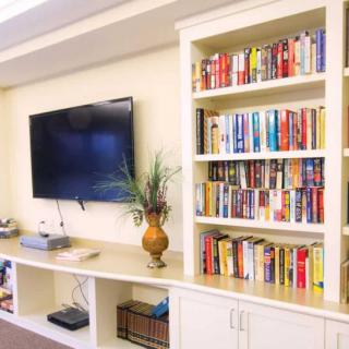 A cozy living room with a large bookshelf filled with books, next to a mounted television.