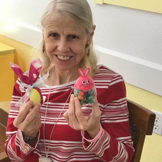 A smiling woman holding handmade bunny decorations indoors.