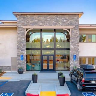 A modern building entrance with a glass facade and stone exterior, accompanied by a parking lot.