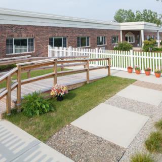 A brick building with a garden, pathway, and white picket fence.