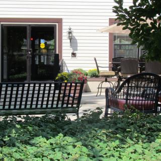 A cozy outdoor patio with benches, chairs, and lush greenery.
