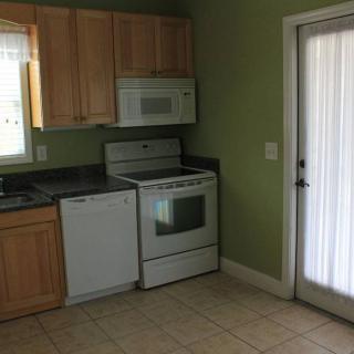 A domestic kitchen featuring appliances such as an oven, microwave, and dishwasher, with wooden cabinets and green walls.