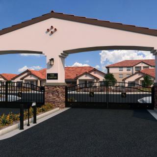 Entrance to a gated residential community with a secure gate and houses in the background.