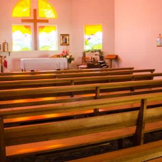 A serene church interior featuring wooden pews and a cross by stained glass windows.