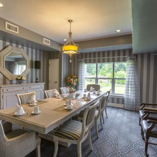 A stylish dining room with a long table and chairs, featuring striped wall decor and a large window providing natural light.