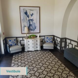 A cozy vestibule with elegant decor, featuring two chairs, a patterned rug, and a piece of wall art.