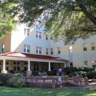 A multi-story residential building surrounded by trees and a garden, with people enjoying the outdoor space.