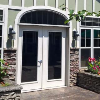A set of glass double doors with a stone facade and surrounding plants.