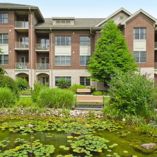A view of an apartment building with a scenic pond and lush greenery in the foreground.
