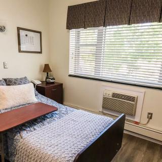 A cozy bedroom with a single bed, bedside table, and a window letting in natural light.