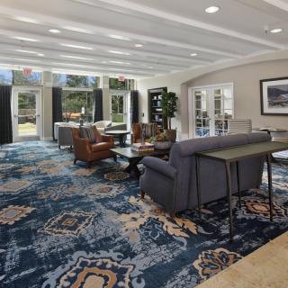 A spacious and well-lit lobby with comfortable seating and large windows, featuring a patterned carpet and stylish furniture.