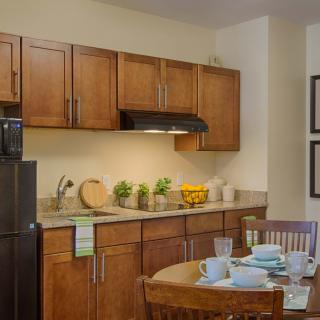 A modern kitchen interior featuring wooden cabinets, a dining table set with tableware, and various kitchen appliances.