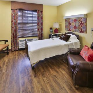 A comfortable hospital room featuring a single patient bed, wooden flooring, and warm decor.