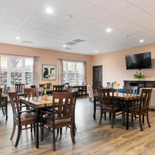 A bright dining room with several tables and chairs, featuring a television and windows.