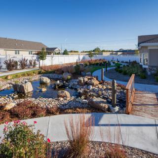 A beautifully landscaped garden with a pond, rocks, and a wooden bridge in a residential area.