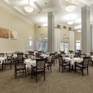 An elegant dining room with neatly arranged tables and chairs, featuring white tablecloths and ambient lighting.
