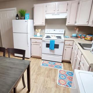 A cozy kitchen with white cabinets and appliances, featuring a dining table and colorful decor.
