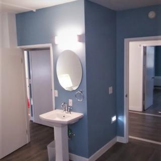 A small bathroom with blue walls, a pedestal sink, and a round mirror.