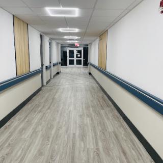 A long, empty hallway with modern lighting and wooden flooring, leading to glass doors.