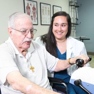 A healthcare professional assists an elderly man during a physical therapy session.