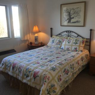 A cozy bedroom with a floral bedspread, bedside lamps, and a framed artwork above the bed.